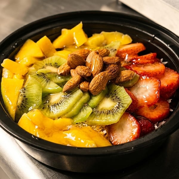 Colorful fruit bowl with mango, kiwi, strawberries, and almonds on a metal counter.